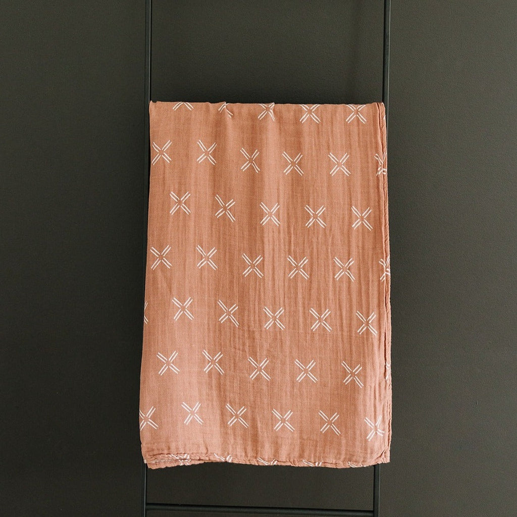 Just Peachy Muslin Swaddle by Mebie Baby hanging on black rod against black wall 