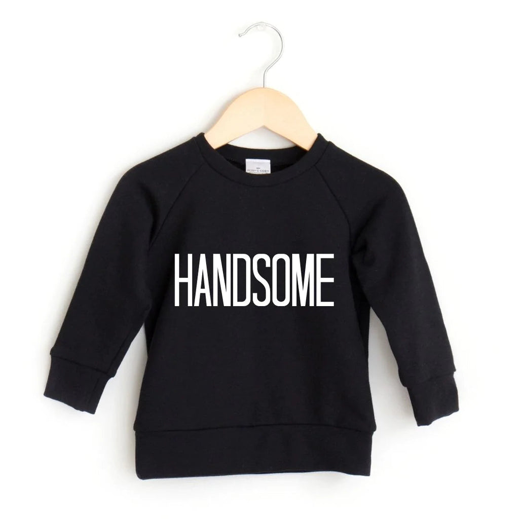 White background with a wooden hanger, and the Handsome Crewneck in Black by Posh and Cozy. Crewneck is black with text in bold white that says "HANDSOME".