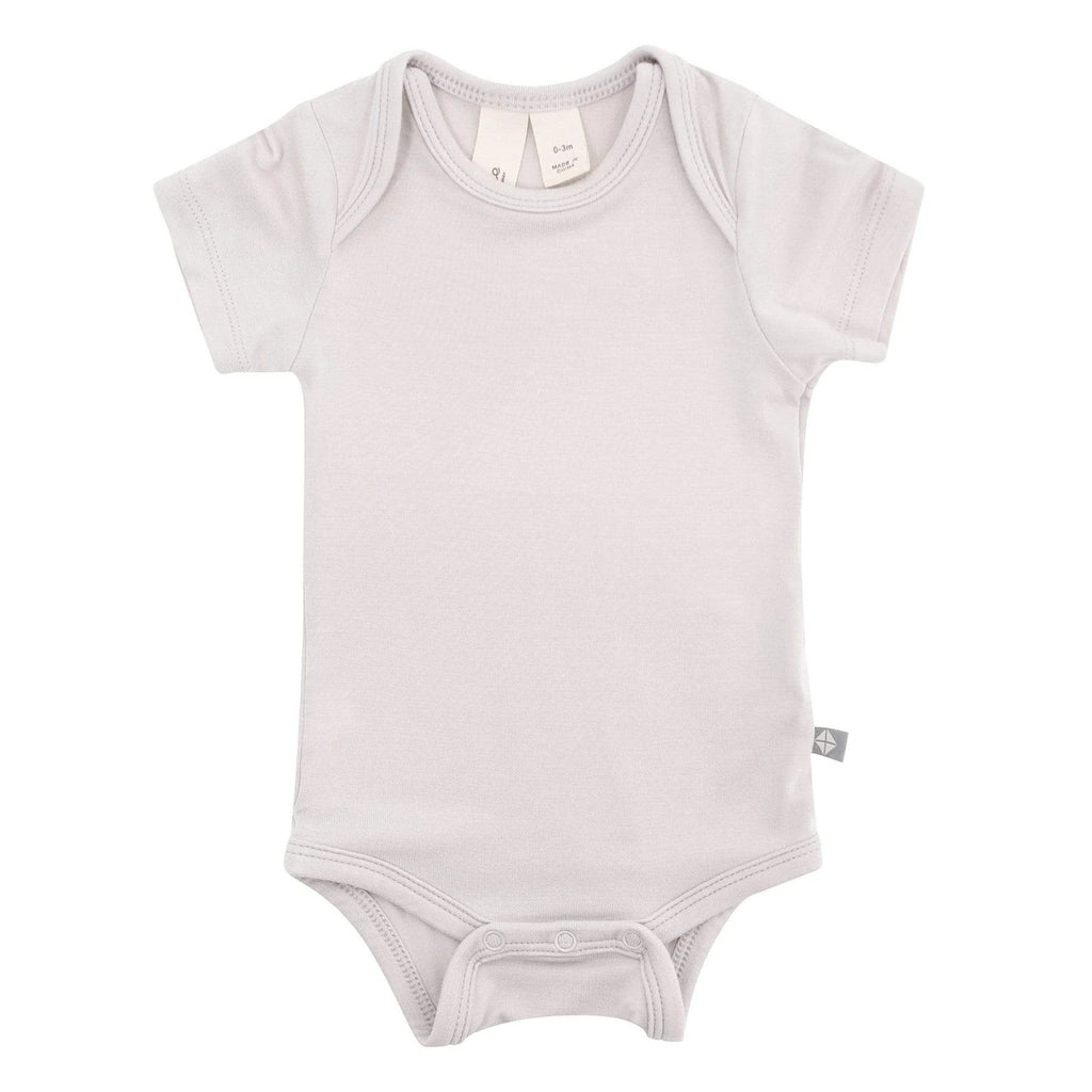 White background with Bodysuit in Oat by Kyte Baby. Oat is a neutral/grey with snap closure on the bottom.