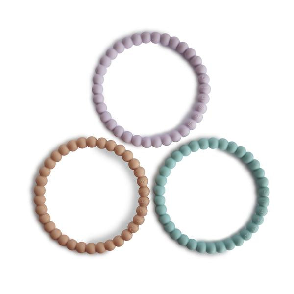 White background with Pearl Teething Bracelet 3-Pack in Lilac/Cyan/Soft Peach by Mushie. These are bracelets with a pearl style bead, in 3 different colours; a peach, lilac, and a medium blue.