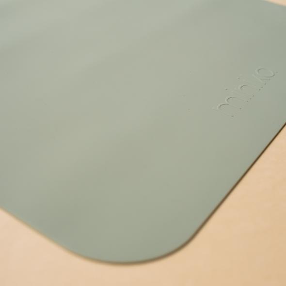 Beige background with a Silicone Placemat in Sage by Minika. Placemat is square silicone, in a sage colour.