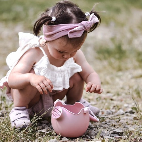 Little girl kneeling outside in the grass, with the Scrunch Watering Can in Blush by Scrunch Kids.